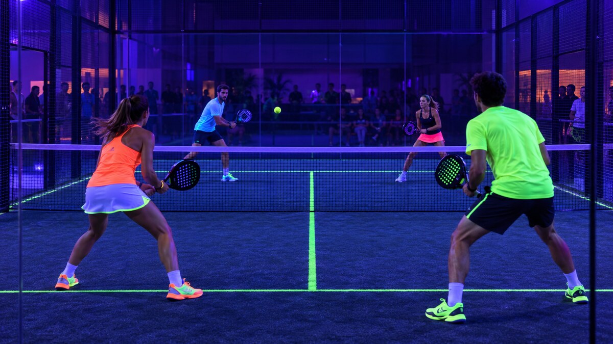 Tournoi de padel fluo en double sur une piste vitrée éclairée par lumière noire UV